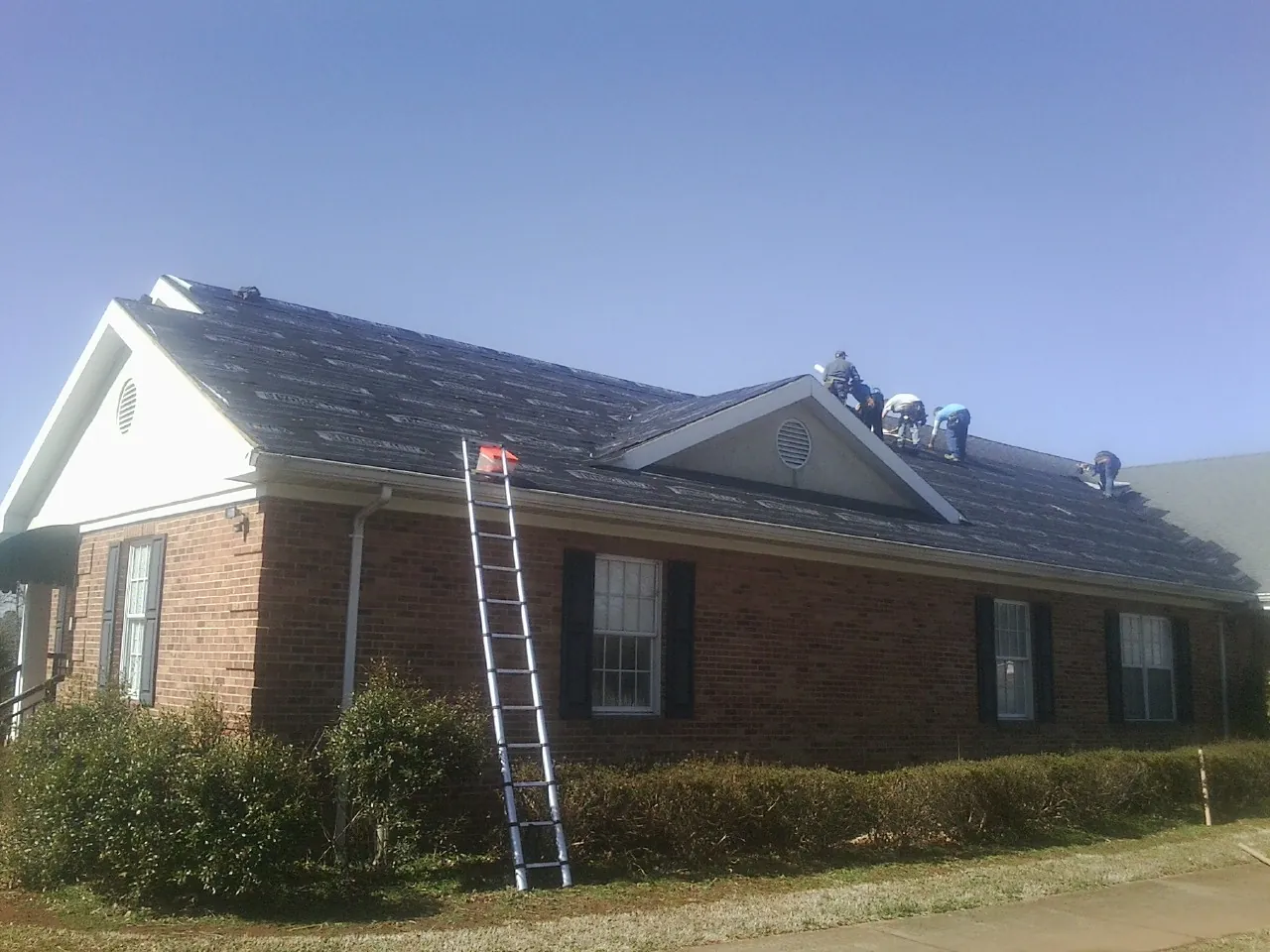Crew tearing shingles off a brick ranch roof with a ladder set — Emergency Roof Repair work by our crew in Shalimar