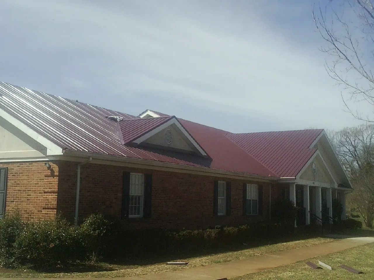 Red metal roof with gabled entries on a long brick building, from a Hail Damage Roof Repair job in Shalimar
