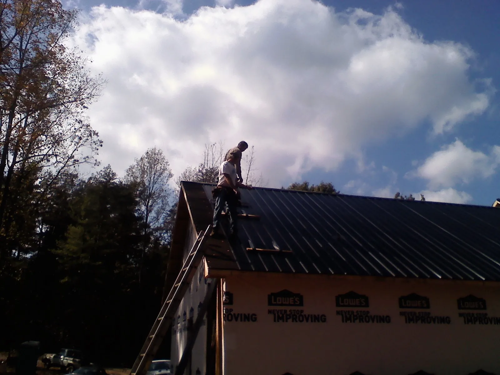Roofer fastening dark metal panels high against a cloudy sky, from a Roof Inspection job in Shalimar