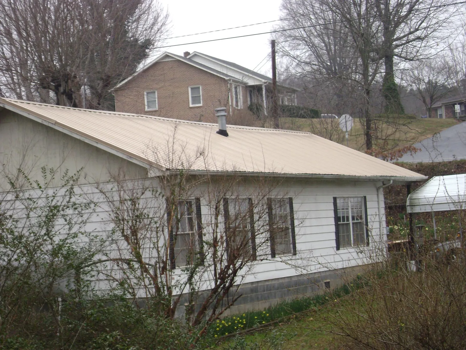 Tan metal roof on a white sided house set into a hillside — Commercial Roofing by Roofing Brothers in Shalimar